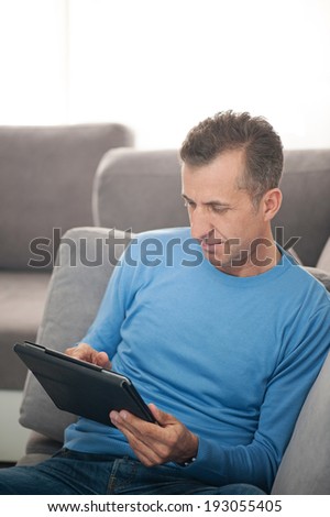Happy man relaxing on sofa with digital tablet - vertical