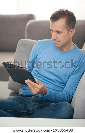 Happy businessman relaxing on sofa with digital tablet - vertical