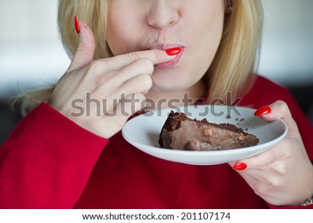 Beautiful girl enjoys eating a cake with chocolate and sucking her finger