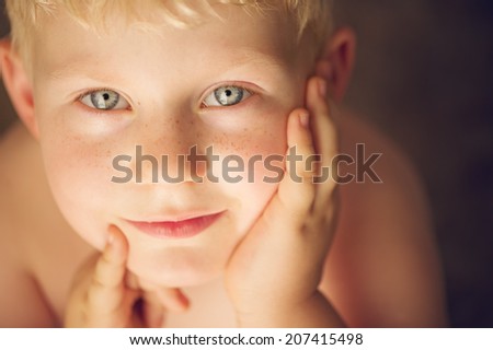 Cute young boy looking up with blond hair and hands close to the face