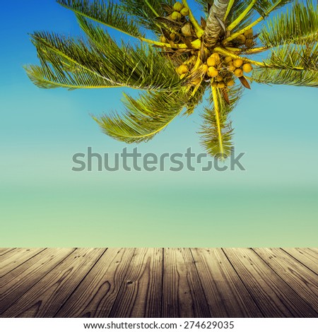 Vintage effect (retro style). Empty wooden table, coconut palm tree, ocean and blurry beach. Tropic island background.