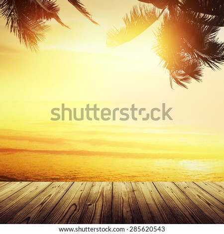 Golden tropical banner background. Empty wooden table and sunset over the ocean. Coconut palm silhouette.
