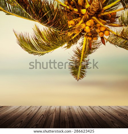 Tropical beach banner background. Coconut palm tree and blurry ocean. Empty wooden table.