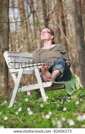 Woman sitting on a sofa in the wood in springtime. She is reading a magazine in the sunlight