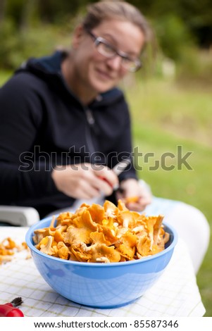 Blue bowl with fresh, picked chanterelles. Woman is rinsing the fungus in background