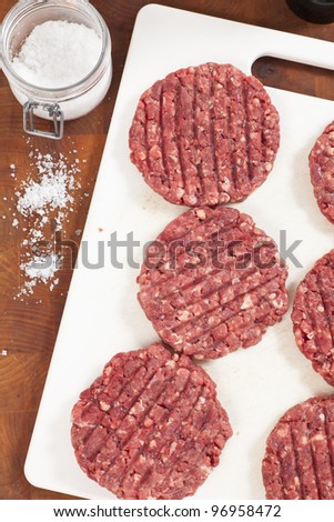 Raw hamburgers on a board with salt beside them