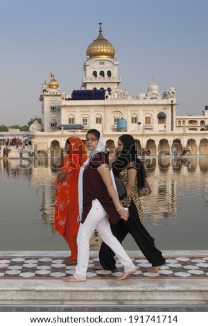 DELHI, INDIA, APRIL 21, 2013: Stylish young women passing by the large holy pond at the Gurdwara Bangla Sahib in Delhi. The water is considered holy by Sikhs who travel there to worship.