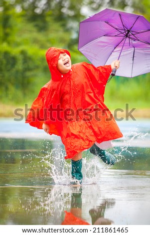 A boy wearing a red raincoat rain jumping happily.