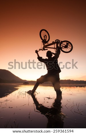 Silhouettes men lift the bike over the lake.