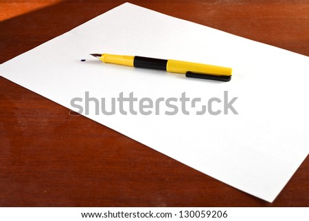 sheet of paper, feather and blot on a wooden table