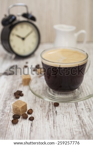 coffee and alarm clock on a table, selective focus on a cup edge