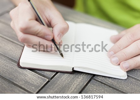 Young man writing notes on a notebook with a pen, close-up view of hands
