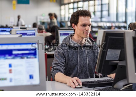 Smiling student using a computer in a library to perform some researches for high school