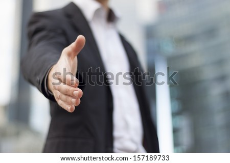 Businessman with an open hand ready to seal a deal with buildings background