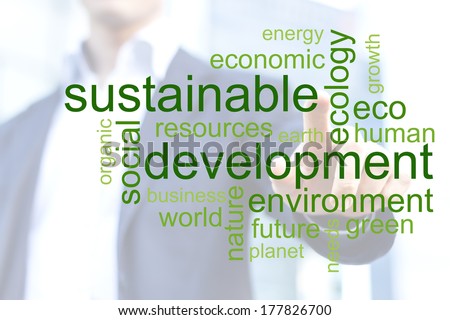 Businessman touching green tag cloud about sustainable development with office buildings in background