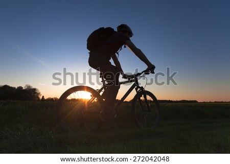 Young adult riding cross-country bicycle at sunset