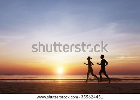 Silhouette of two sportive runners running on the beach at sunset, concept about healthy lifestyle and well-being