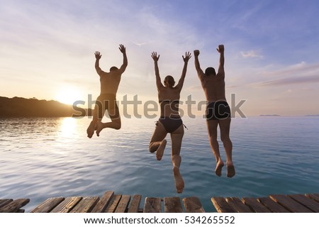 Group of happy people having fun jumping in the sea water from a pier