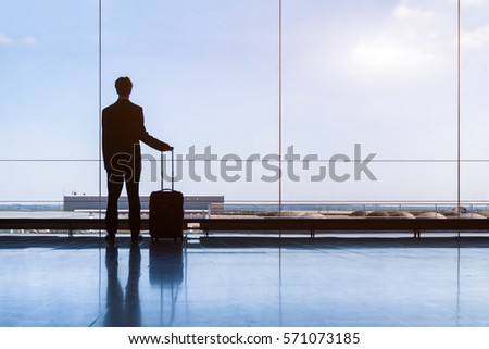 Traveler businessman in airport lounge waiting for the flight and standing with trolley luggage, business travel