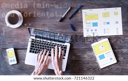 Webdesigner sketching responsive website wireframe mockup with laptop, smartphone and digital tablet computer on wooden table, UI and UX front end development concept, top view
