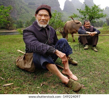 YANGSHUO COUNTY, GUANGXI, CHINA - MARCH 29: Elderly Chinese shepherds in green gumshoes, graze cattle near the Lijiang River, against the backdrop of karst hills, march 29, 2010. Guilin neighborhood.