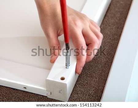 Assembling furniture in the home, screwing connecting dowels, using a Phillips screwdriver. White furniture panel.