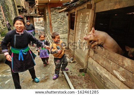 GUIZHOU PROVINCE, CHINA - APRIL 13: The family of Chinese peasants with kids, pass past the pigsty, April 13, 2010. Asian peasant farming, pig farming, animal husbandry, rural south-west China.
