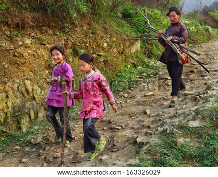 GUIZHOU PROVINCE, CHINA - APRIL 11: Chinese family descends rocky mountain path, two girls are 8 years old, and their mother, farmer, peasant, holding bundle of firewood in his hands, April 11, 2010.