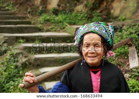 PINGAN VILLAGE, GUANGSI PROVINCE, CHINA - APRIL 5:  Elderly farmer peasant woman coming down the mountain, the steps of stone stairs, with a hoe on her shoulder, April 5, 2010.