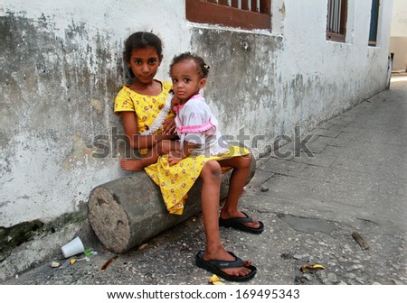 ZANZIBAR, TANZANIA - FEBRUARY 16: Tanzania, Zanzibar island, Stone Town,  dark-skinned African girl 8 years old, sitting on  log near house, she holds in her lap sister 2 years old, February 16, 2008.