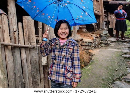 YAO VILLAGE DAZHAI, LONGSHENG, GUANGXI PROVINCE, CHINA - APRIL 3, 2010: Unknown Asian girl, about 8 years old, holding a blue umbrella over his head and laughs. Countryside southwestern China
