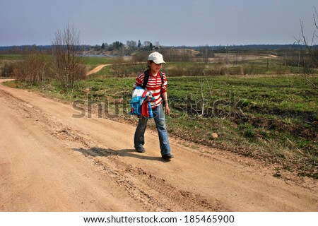 Tver, Russia - May 5, 2006: Rural areas in Russia, village girl 11 years old goes from rural school, home, on long winding country road on  girl white cap, jeans and jacket, with white and red stripes