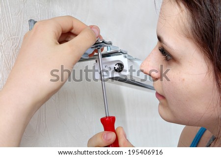 Girl mounts vertical blinds on the wall,  tighten screw red screwdriver