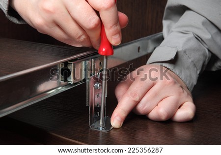 Assembling of furniture, Installing Computer desk keyboard tray track drawer slide rail, screwing screw manual screwdriver.