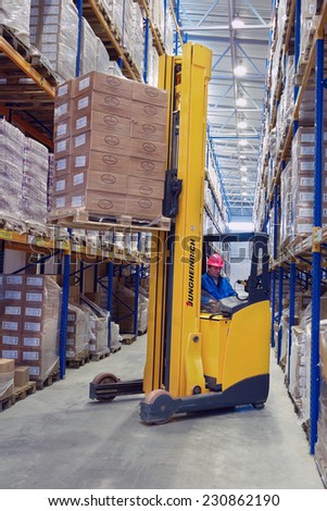 St. Petersburg, Russia - November 21, 2008: Yellow Forklift pallet truck lifts the pallet in the narrow aisle warehouse. Forklift raises palletising on top shelf of the rack.