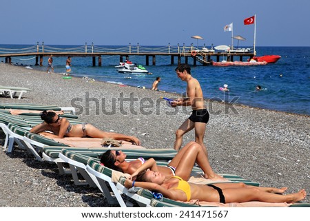 Kemer, Turkey - August 29, 2014: Unidentified men and women sunbathing on the private pebble beach resort of Antalya, the beach is equipped with sun loungers and a berth for boats, summer, sunny day.
