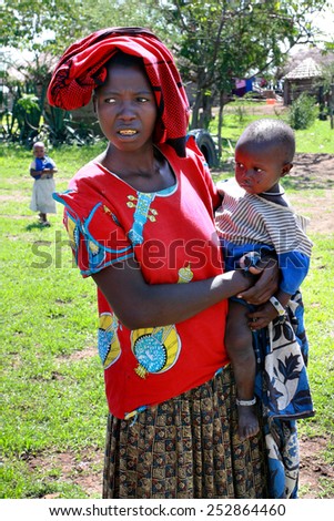 Meserani Snake Park, Arusha, Tanzania - February 14, 2008:  African Maasai tribe village, a black woman in red clothes of humanitarian aid, holds on hands a baby.