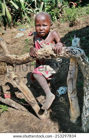 Meserani Snake Park, Arusha, Tanzania - February 14, 2008: Unknown black African child of the Maasai tribe, about four years old, boy or girl, standing in front of the kitchen garden fence.