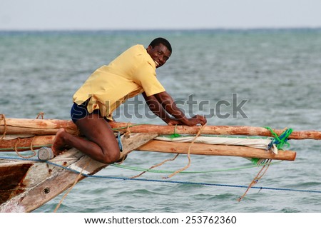Zanzibar, Tanzania - February 18, 2008: Black African fisherman in yellow T-shirt, fixes rigging small wooden fishing sailing vessel.