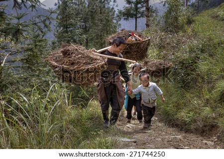Langde Village, Guizhou, China - April 15, 2010: Peasants carrying a heavy load on their shoulders,  and holding the hand of a boy about 5 years old.