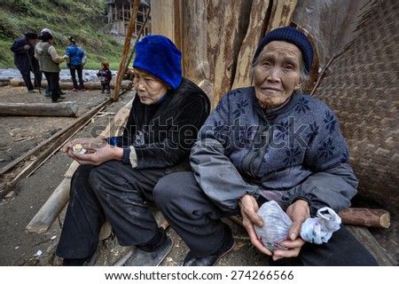 Langde Village, Guizhou, China - April 16, 2010: Two elderly Chinese woman peasant, rural women, sitting near  farmhouse new buildings to rustic celebration. Kaili Langde Miao Ethnic Minority Village