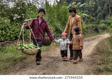Yang Di village, Yangshuo, Guangxi, China - March 29, 2010: On country road in farmland is walking asian family, women and children, farmer carries on his shoulder a pole counterbalance to two baskets