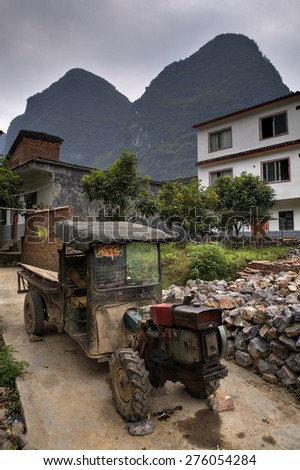 Yangshuo, Guangxi, China - March 29, 2010: Worn vintage farm tractor stands under the open sky in a peasant village, amid the karst hills of Guilin and Yangshuo, near the farmhouse,  southern China.