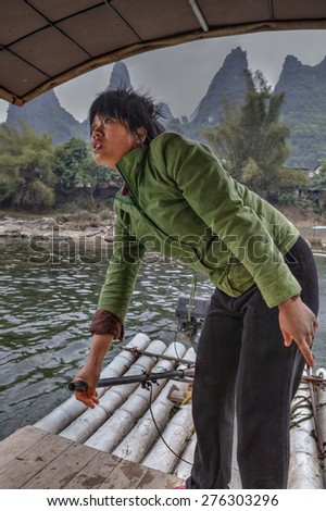 Yang Di village, Yangshuo, Guangxi, China - March 29, 2010: Chinese boatmen women Lijiang River, bamboo raft with an outboard motor, ferryman Asian girl in a green jacket, operates ferry.
