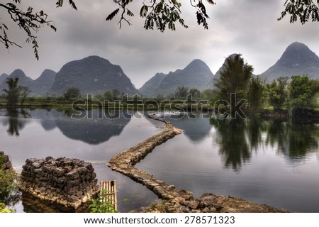 The dam on the river Yulong in spring, at low water, amid the picturesque countryside of Guilin, with peaks of karst hills, Yangshuo County, Guangxi Province, southwest China.