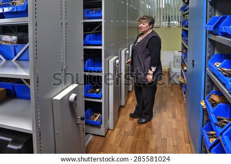 St. Petersburg, Russia - May 21, 2015: Mobile Compactor Storage System on rails, Toolroom, Woman storekeeper moves mobile shelving storage of tools on  guide paths.