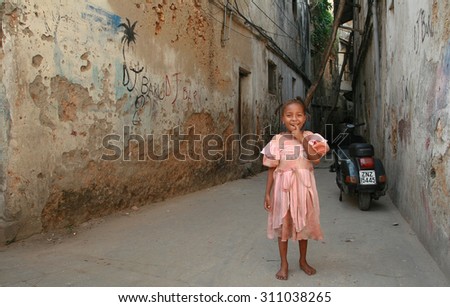 Zanzibar, Tanzania - February 16, 2008: Unknown smiling African girl with braids around 6 years old, standing near the old dilapidated, stone houses.