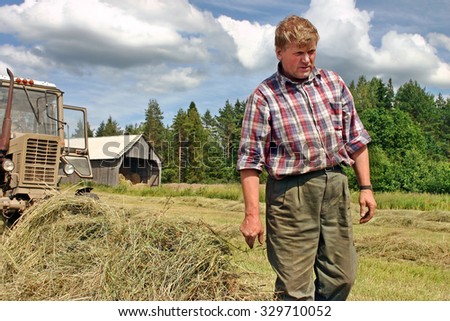 Lemozero, Olonets, Karelia, Russia - July 26, 2006: Harvesting hay in the Russian north, the farmer tractor-driver inspecting the field before the start of hay baler.