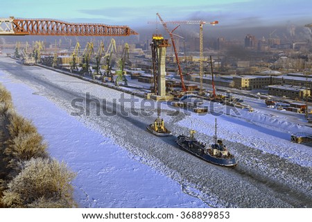 St.Petersburg, Russia - January 23, 2016: Top view of the ice-bound sea channel with passing boats, cargo port and harbor cranes, winter daytime.