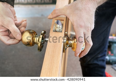 Door installation, worker Installs door knob, woodworker hands close-up.